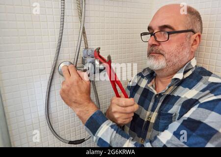 Plumber with pipe wrench mounts new shower hose on the shower in the bathroom Stock Photo