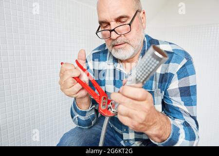 Plumber handyman with pipe wrench repairing the shower head and hose in the bathroom Stock Photo