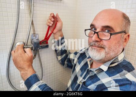 Plumber handyman me pipe wrench assembles new hose on the shower in the bathroom Stock Photo