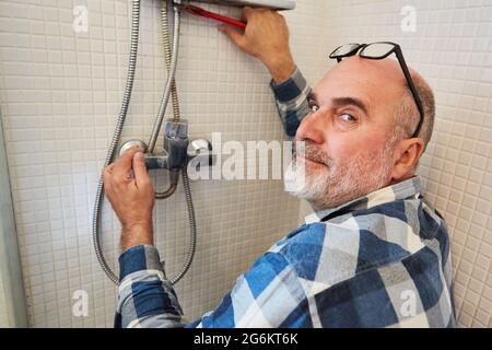 Plumber handyman repairs or assembles shower hose in shower in bathroom Stock Photo