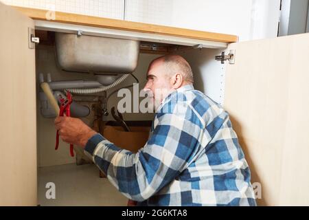 Plumber craftsman with pipe wrench repairs the drain on the kitchen sink Stock Photo