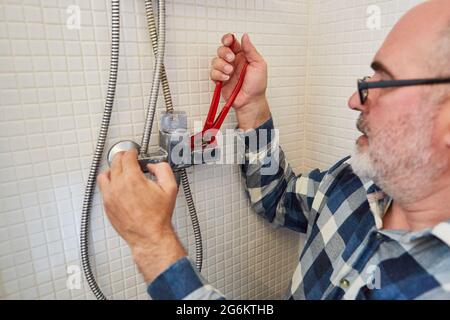 Handyman as a plumber with pipe wrenches assembles new shower hose in the shower Stock Photo