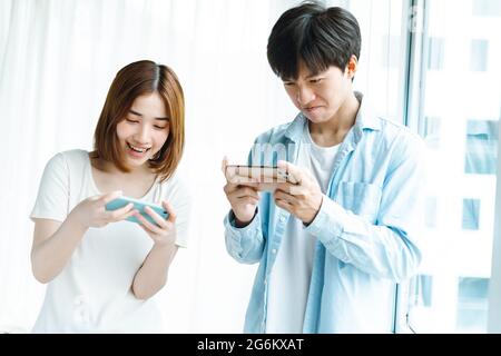 Young Asian couple playing games together on mobile phones Stock Photo