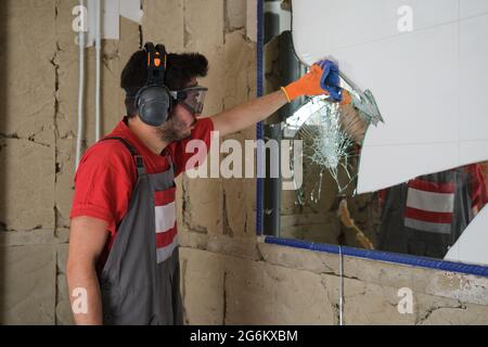 Builder removing a mirror from a wall. House renovation. Stock Photo