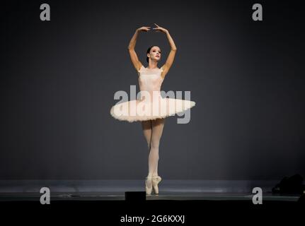Beautiful dancer in classical pose, tutu and pointe shoes on the stage during a performance or rehearsal Stock Photo