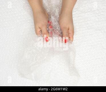 female hand holding crumpled piece of polyethylene with air bubbles on a white background, packing material, top view Stock Photo