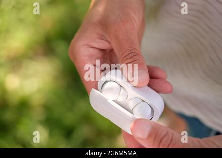 Woman hand open a case with wireless headphones, outdoors, in the blurry background.  Stock Photo