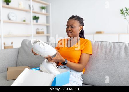 Dissatisfied woman opening box from online shop and looking at wrong delivered item, unhappy with received sneakers Stock Photo