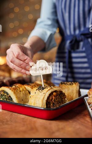 Sales Assistant In Bakery Putting Vegetarian Free Label Into Freshly Baked Savoury Roll Stock Photo