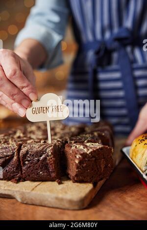 Sales Assistant In Bakery Putting Gluten Free Label Into Freshly Baked Chocolate Brownies Stock Photo
