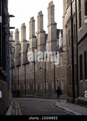 One person walking along the narrow lane lined old buildings with with tall Trinity college chimneys in Trinity Lane Cambridge England Stock Photo