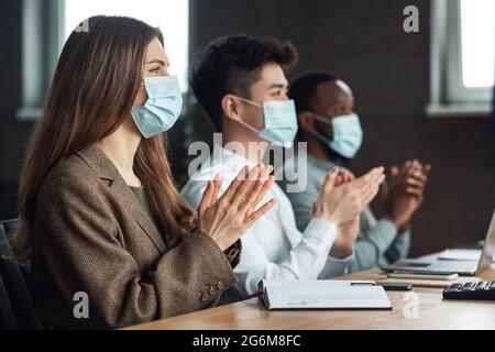 Colleagues in masks having meeting in boardroom, clapping hands Stock Photo