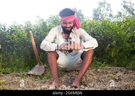 Indian Young Farmer Using Smart Phone Sitting in their agriculture field Stock Photo