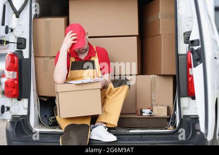 Tired man courier sitting on car with cardboard boxes with documents in his hands Stock Photo