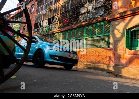 KOLKATA, WEST BENGAL, INDIA - DECEMBER 24TH 2017 : Big shadow of a tree on red wall of a house of Bow Barracks, Kolkata. A modern car approaching. Stock Photo