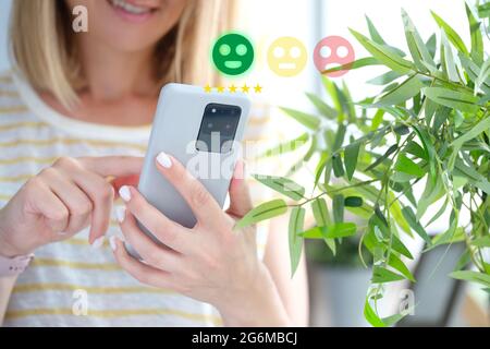 Woman pressing smiley face emoticon on mobile phone closeup. Customer service evaluation concept Stock Photo