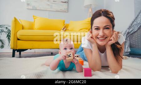 happy mother looking at camera while infant son playing with toys Stock Photo