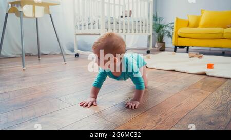infant boy crawling on floor near feeding chair in living room Stock Photo