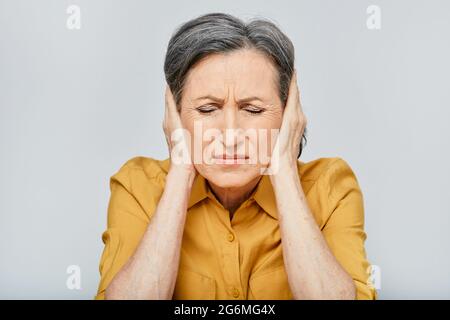 Headache, stress. Mature woman with headache touching hands on temples with suffering facial and eyes closed. Migraine Stock Photo
