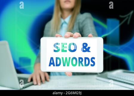 Conceptual display Seo And Adwords. Word for they are main tools components of Search Engine Marketing Business Woman Sitting In Office Holding Mobile Stock Photo