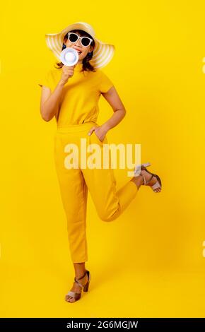 Cute and funny Asian woman in yellow casual cloth style and wearing hat holding white megaphone for announcement and show hand to present product Stock Photo