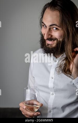 Portrait of a young middle eastern businessman with beard and long hair laughing cheerfully while holding a wineglass Stock Photo