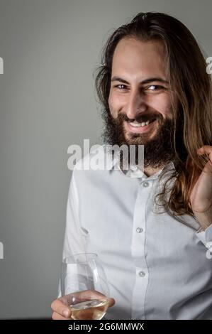 Portrait of a young middle eastern businessman with beard and long hair laughing cheerfully while holding a wineglass Stock Photo