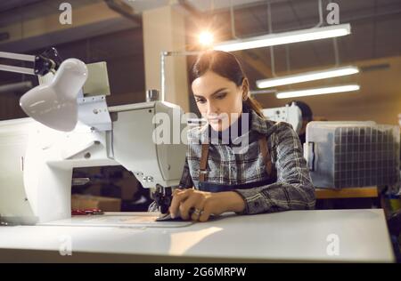 Woman working at table with industrial sewing machine at shoe or clothing factory Stock Photo