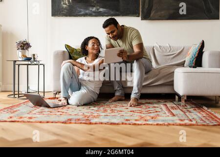 Middle eastern man and woman talking while using tablet computer and laptop at home Stock Photo