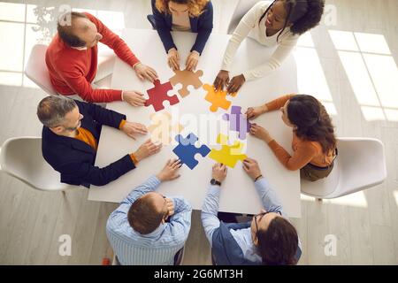 Creative business team sitting around office table and trying to put jigsaw pieces together Stock Photo