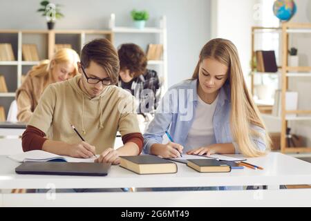 Diverse students at shared desk making notes studying together at university Stock Photo