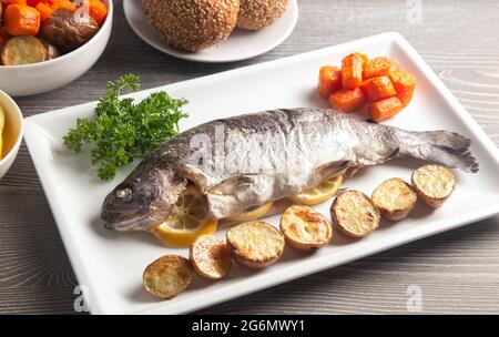 A Whole Baked Rainbow Trout on a Table Set for Dinner Stock Photo