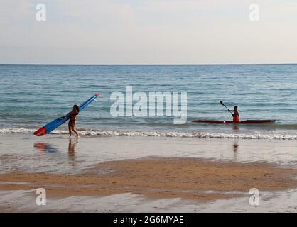 Young woman carrying a surf ski on the beach with a young man preparing to carry his out of the water Sardinero Santander Cantabria Spain Stock Photo