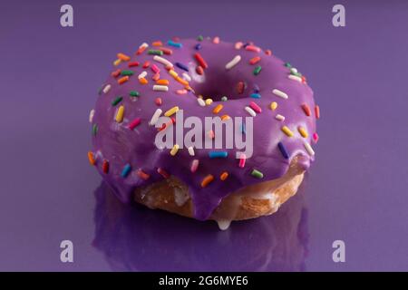 A Purple Glazed Donut with Rainbow Sprinkles on Top Stock Photo