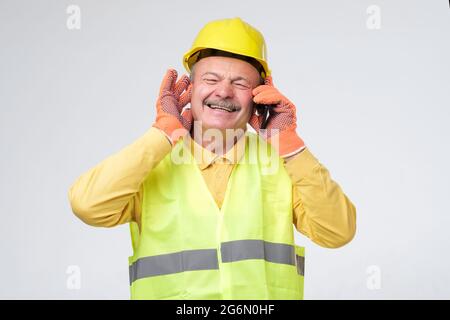 Worker wearing safety helmets close his other ears while talking on mobile phone Stock Photo