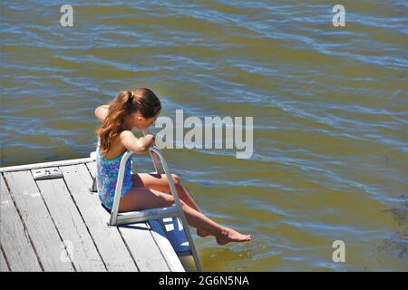 A 7 year old girl is sitting by a lake with fishing rod and looking at the  water. She waits for a fish to bite Stock Photo - Alamy