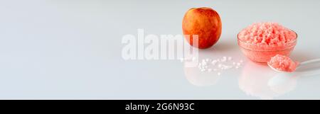 Panoramic banner with creamy salt body scrub and peach in the background, like a concept of smooth skin. Homemade pink color scrub. Homemade Cosmetics Stock Photo