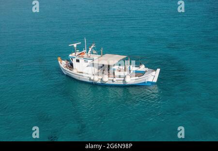 Fishing boat on turquoise blue color sea background. Aerial drone view. Blue and white traditional trawler moored in Aegean rippled water, sunny day. Stock Photo