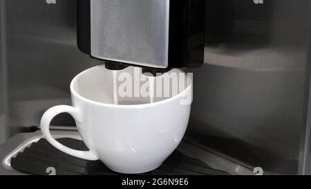 Fully automatic Espresso Maker coffee machine pouring milk in coffee cup. Stock Photo