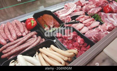 meat department display shelves with selection of typical fresh raw meats slices and variety of sausage products inside market or supermarket refriger Stock Photo