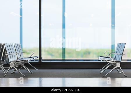 Empty rows of seats in airport waiting area. Chairs in big light hall waiting for passengers to arrive. Trips and travelling. Airfield in background Stock Photo