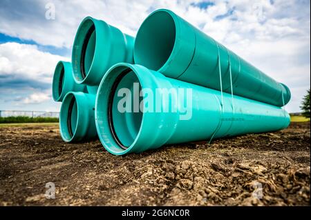 Stacked water main pipe with bell fitting next to an exposed trench for installation Stock Photo