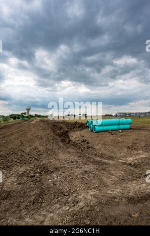 Stacked water main pipe with bell fitting next to an exposed trench for installation Stock Photo