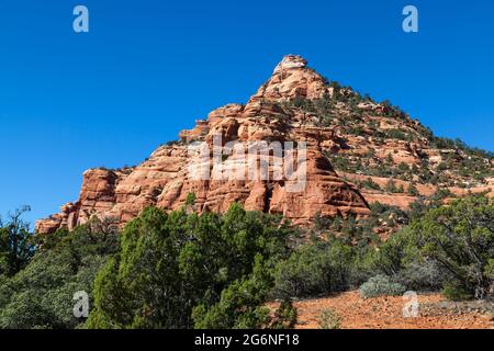 Red layered sandstone eroded over time into a mountain peak and dotted with trees and brush near Zion National Park, Utah. Stock Photo