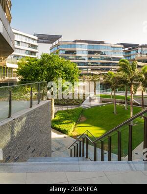 Marble staircase and glass handrail leading to street in contemporary urban city district with well run glass buildings, verdant lawn, and palm trees on sunny day Stock Photo