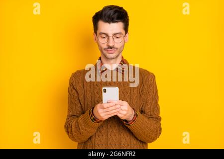 Portrait of concentrated man look phone typing comment wear knitted pullover isolated on yellow color background Stock Photo