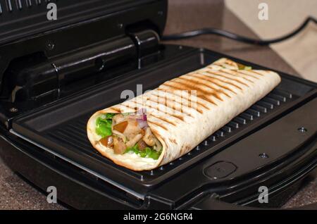 https://l450v.alamy.com/450v/2g6ngr4/roll-of-pita-bread-vegetables-and-chicken-cooking-on-an-electric-grill-kebab-shawarma-2g6ngr4.jpg