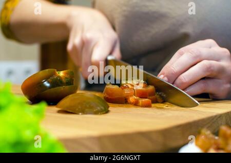 Tomato on a cutting board in the kitchen. A woman chef cuts a black tomato on a wooden cutting board with a knife. Cooking process, close-up. Stock Photo