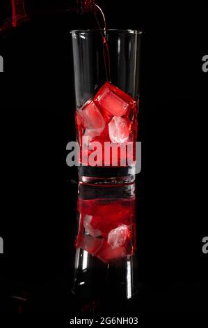 Pouring red juice on the top of the ice into the glass against complete dark background. copy space. Pour alcohol, winery concept. Stock Photo