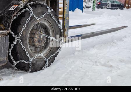 The loader is driving in the snow, the wheels are equipped with chains. Winter snowy day Stock Photo